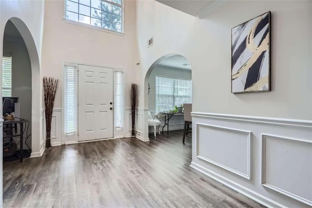 foyer with a wainscoted wall, wood finished floors, visible vents, and a decorative wall