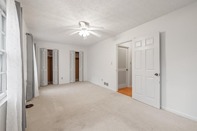 unfurnished bedroom featuring multiple closets, ceiling fan, light carpet, and a textured ceiling