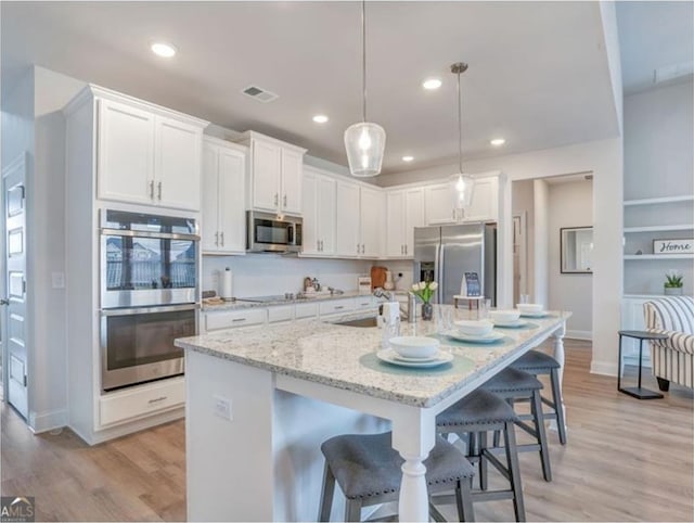 1023 Boulder Dr, Gray, GA 31032 - kitchen featuring a breakfast bar, stainless steel appliances, white cabinets, visible vents, and light wood-style floors