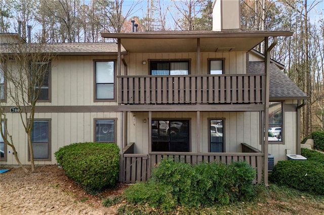 view of front of home with a balcony, covered porch, a shingled roof, board and batten siding, and a chimney