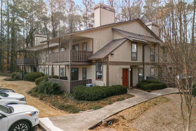 view of front of house with a shingled roof, a chimney, and a balcony