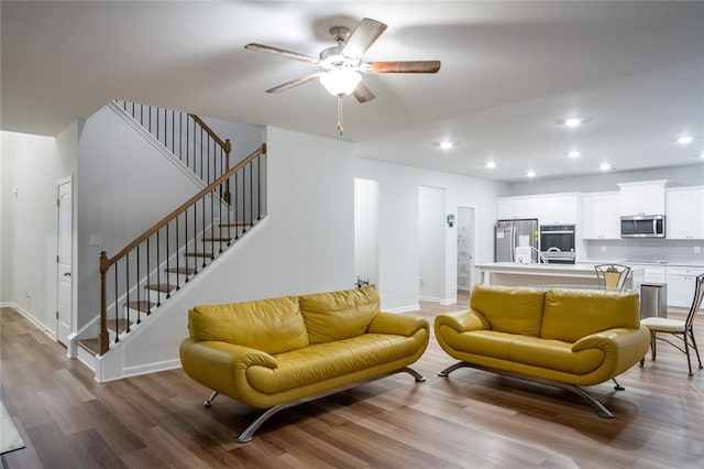 living room featuring light wood finished floors, baseboards, a ceiling fan, stairway, and recessed lighting