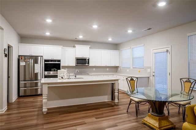 kitchen with a kitchen island with sink, stainless steel appliances, visible vents, white cabinetry, and dark wood finished floors