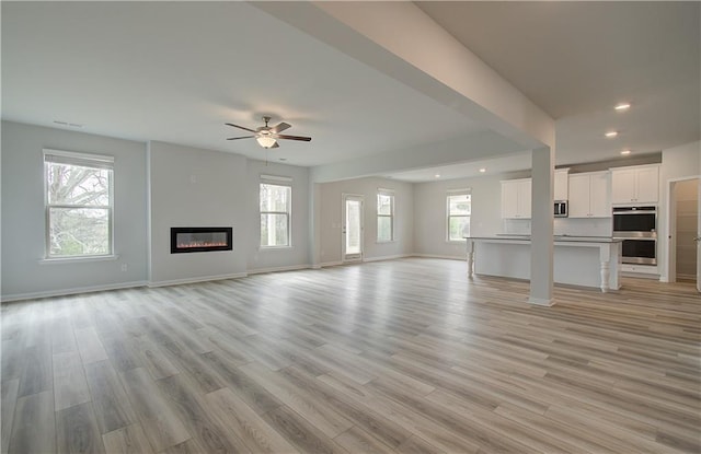 unfurnished living room with light wood finished floors, a wealth of natural light, and a glass covered fireplace