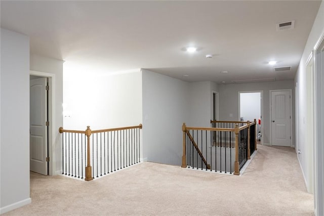 hallway featuring carpet floors, baseboards, visible vents, and an upstairs landing