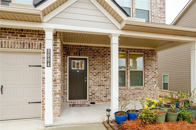 view of exterior entry featuring a porch, an attached garage, and brick siding