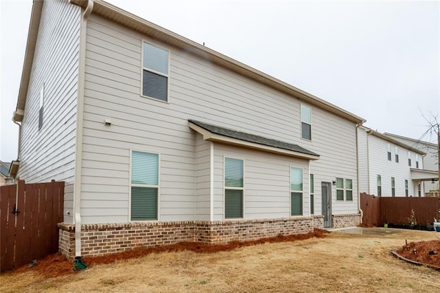 rear view of house featuring brick siding and fence