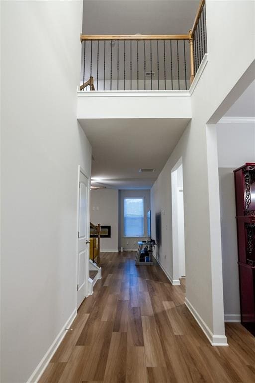 corridor featuring a towering ceiling, stairs, baseboards, and wood finished floors