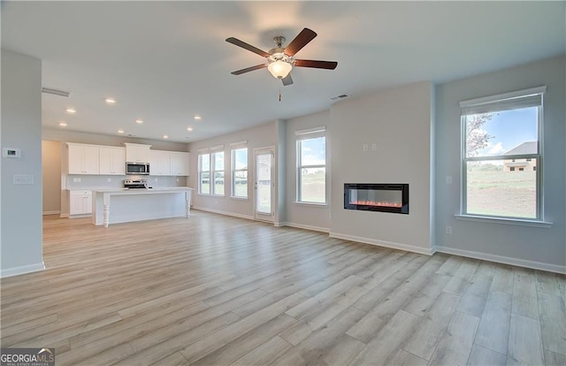 unfurnished living room with recessed lighting, visible vents, light wood-style floors, a glass covered fireplace, and baseboards