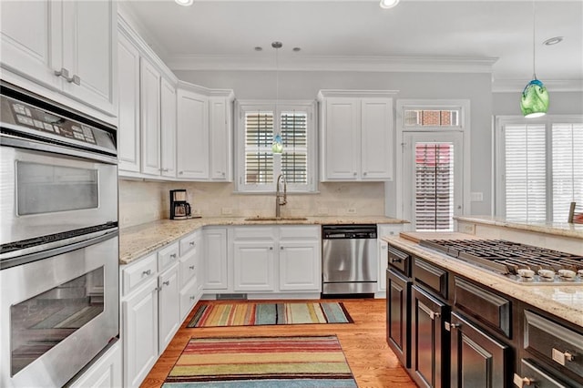 kitchen featuring appliances with stainless steel finishes, a sink, white cabinets, dark brown cabinetry, and crown molding