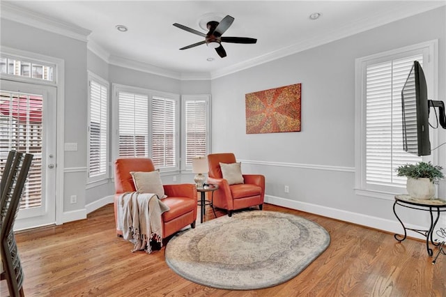 living area featuring wood finished floors, healthy amount of natural light, a ceiling fan, baseboards, and ornamental molding