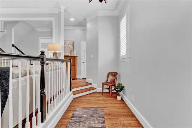 hall with light wood-type flooring, crown molding, an upstairs landing, baseboards, and recessed lighting