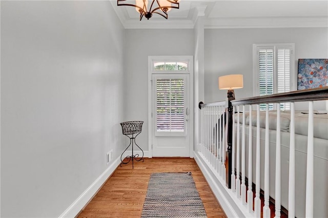 hallway with ornamental molding, light wood finished floors, a chandelier, and baseboards