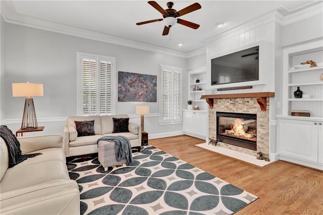 living area with ceiling fan, light wood-style flooring, crown molding, a fireplace, and built in features
