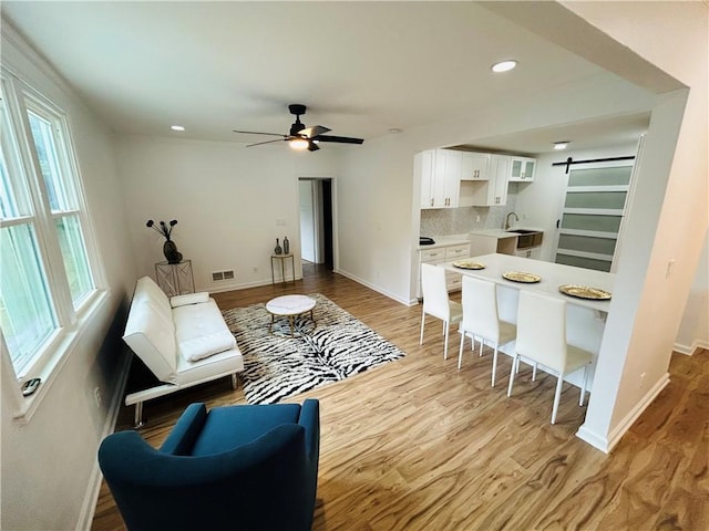 living room featuring light wood-type flooring, recessed lighting, a barn door, baseboards, and ceiling fan