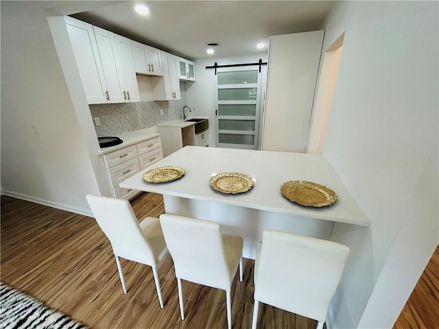 kitchen featuring a breakfast bar, a sink, backsplash, a barn door, and white cabinets