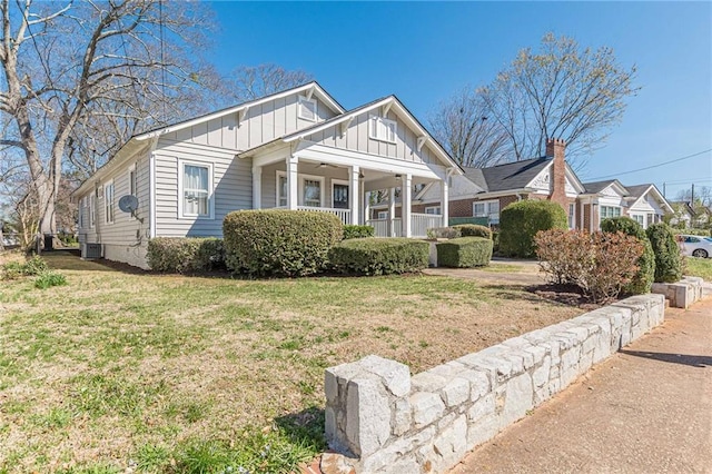 view of front of house featuring covered porch, cooling unit, board and batten siding, and a front yard