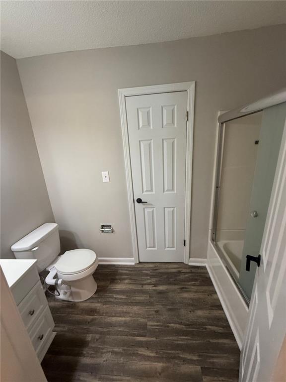 full bathroom with wood-type flooring, shower / bath combination with glass door, vanity, toilet, and a textured ceiling