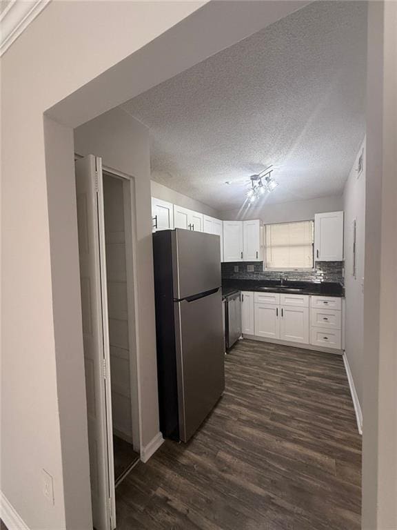 kitchen featuring appliances with stainless steel finishes, tasteful backsplash, white cabinetry, dark hardwood / wood-style flooring, and a textured ceiling