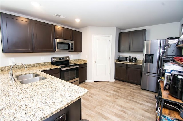 kitchen with sink, light hardwood / wood-style flooring, light stone countertops, dark brown cabinets, and stainless steel appliances