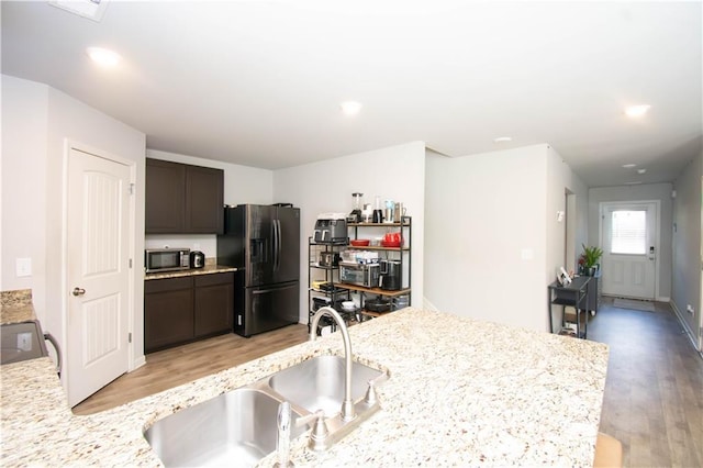 kitchen with sink, light wood-type flooring, dark brown cabinets, light stone counters, and stainless steel appliances