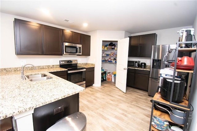 kitchen featuring sink, light stone countertops, light wood-type flooring, appliances with stainless steel finishes, and dark brown cabinets