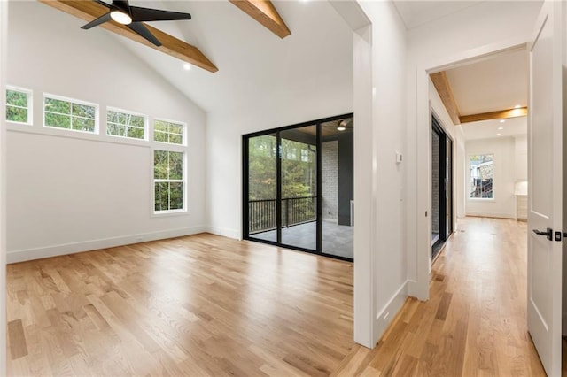 empty room with ceiling fan, a healthy amount of sunlight, beam ceiling, and light hardwood / wood-style flooring