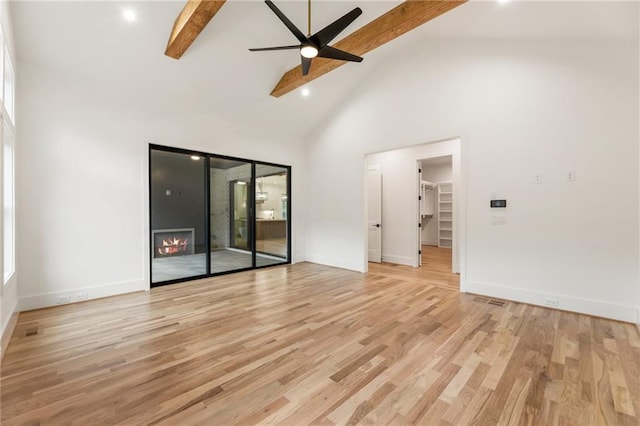 unfurnished living room featuring ceiling fan, beam ceiling, light hardwood / wood-style flooring, high vaulted ceiling, and a fireplace