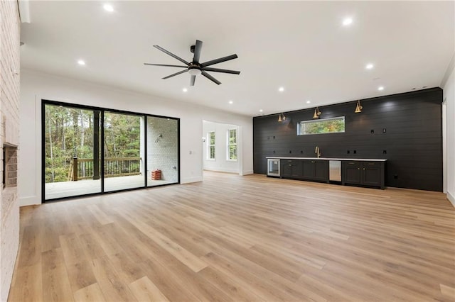 unfurnished living room with light hardwood / wood-style floors, ceiling fan, wooden walls, and sink