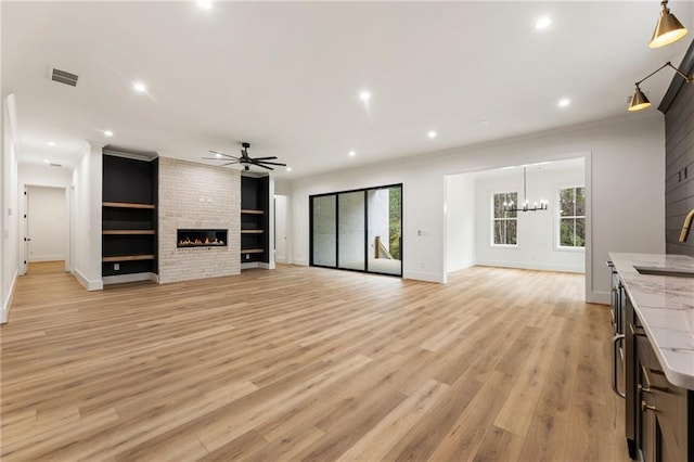 unfurnished living room with sink, light wood-type flooring, a fireplace, ceiling fan with notable chandelier, and ornamental molding