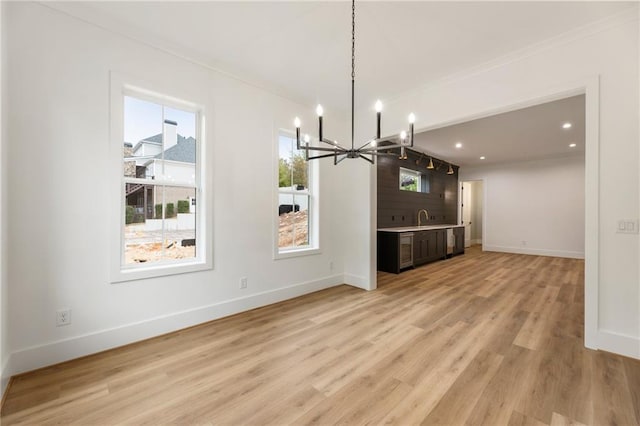 unfurnished living room with sink, light hardwood / wood-style flooring, and an inviting chandelier