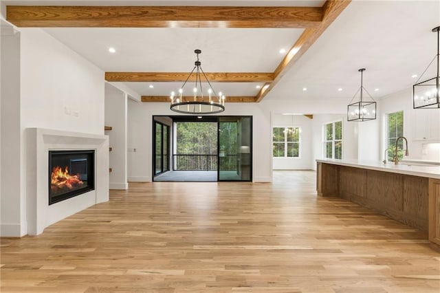 unfurnished living room featuring beamed ceiling, light wood-type flooring, and sink