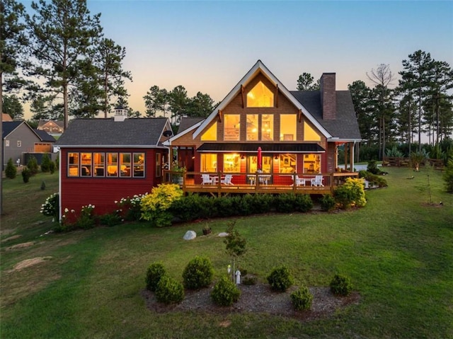 back house at dusk with a lawn and a deck