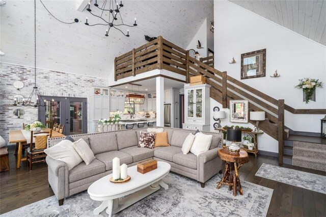 living room with a notable chandelier, brick wall, high vaulted ceiling, and hardwood / wood-style floors