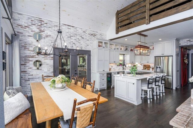 dining room featuring a chandelier, wine cooler, dark wood-type flooring, a high ceiling, and brick wall