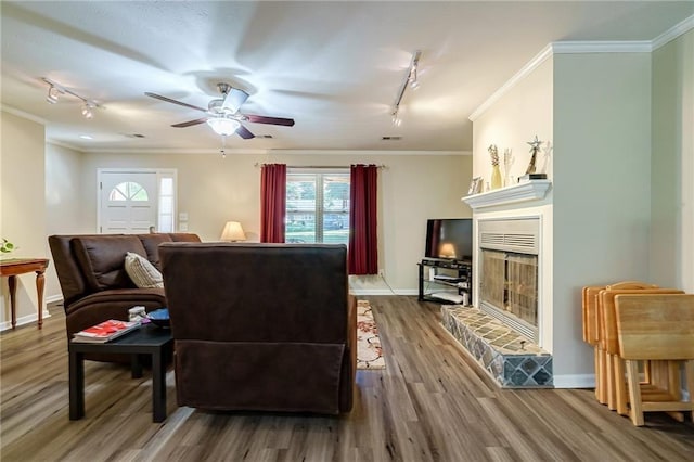 living room featuring ceiling fan, ornamental molding, wood-type flooring, rail lighting, and a fireplace