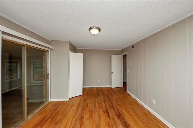 empty room featuring crown molding, light hardwood / wood-style floors, and a textured ceiling