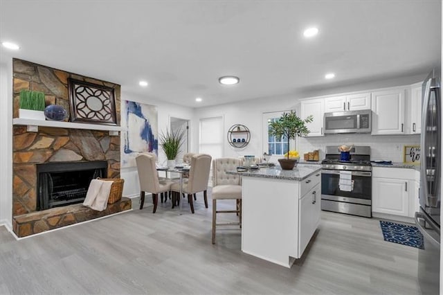 kitchen with white cabinets, a kitchen island, appliances with stainless steel finishes, a fireplace, and backsplash