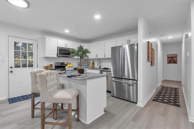 kitchen with a center island, a breakfast bar area, stainless steel appliances, light wood-style floors, and white cabinetry