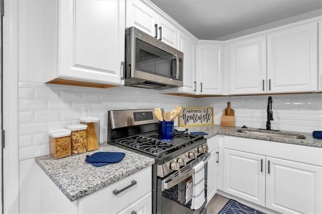 kitchen featuring decorative backsplash, white cabinetry, stainless steel appliances, and a sink