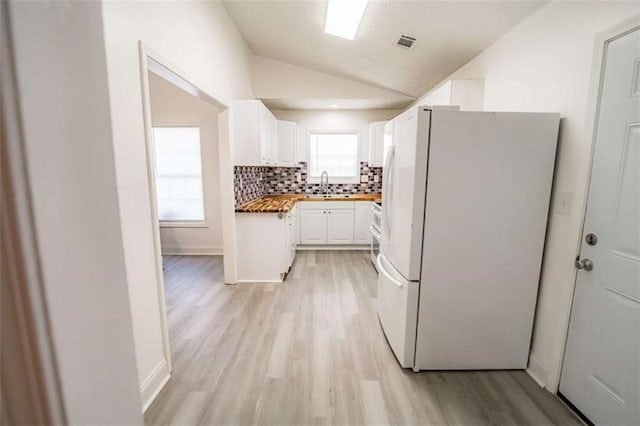 kitchen with white cabinets, a sink, freestanding refrigerator, backsplash, and vaulted ceiling