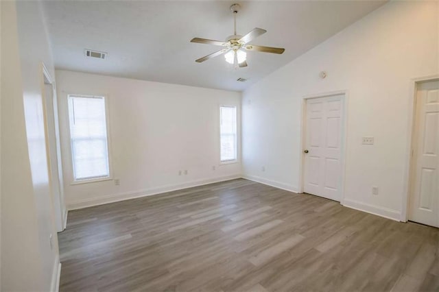 spare room with ceiling fan, visible vents, vaulted ceiling, wood finished floors, and baseboards