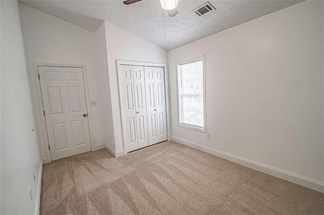 unfurnished bedroom with visible vents, lofted ceiling, baseboards, a textured ceiling, and carpet flooring