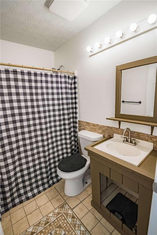bathroom with a shower with curtain, a textured ceiling, tile patterned flooring, vanity, and toilet
