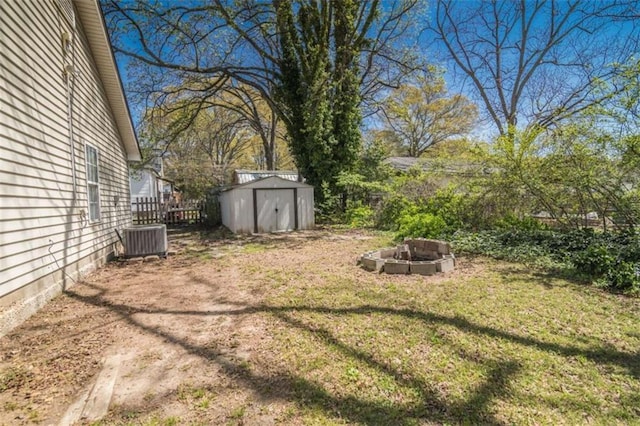 view of yard with fence, a storage unit, an outbuilding, central air condition unit, and a fire pit
