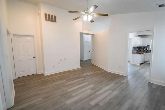empty room with a ceiling fan, dark wood-style flooring, visible vents, baseboards, and high vaulted ceiling