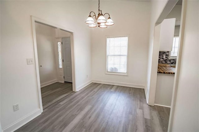 unfurnished dining area with dark wood-style flooring, baseboards, and a notable chandelier