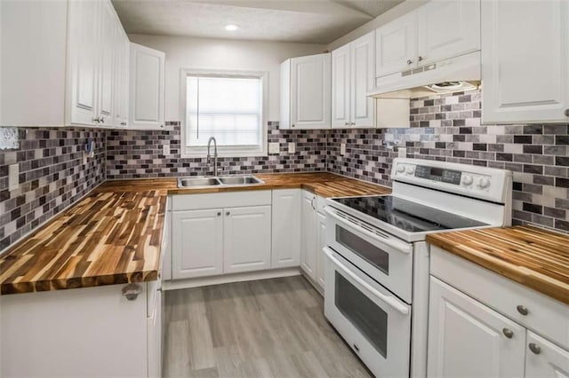 kitchen with a sink, white cabinetry, double oven range, under cabinet range hood, and butcher block counters