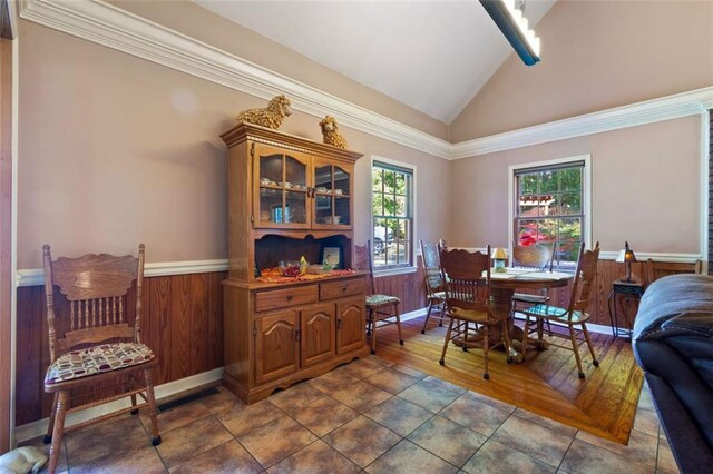 dining room featuring dark tile patterned floors, vaulted ceiling, and wood walls