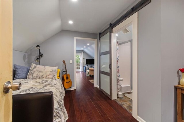 bedroom featuring lofted ceiling, dark hardwood / wood-style flooring, connected bathroom, and a barn door